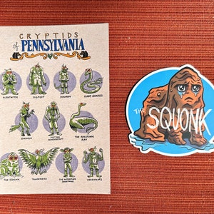 May include: A brown and green illustrated card with the title "Cryptids of Pennsylvania". The card features illustrations of various cryptids, including the Squonk, the Thunderbird, the Albatwitch, and the Giant Snakes. A separate sticker features a cartoon illustration of the Squonk, a brown creature with a sad expression.