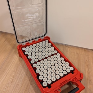 May include: Open red plastic tool case filled with numerous cylindrical objects. The case has a clear lid with the Milwaukee logo. The handle is black and the case is sitting on a wooden floor.