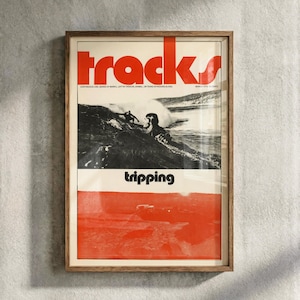 May include: Framed vintage "tracks" magazine cover. The poster features the word "tracks" in large red letters. Below the title is a black and white image of people surfing. The bottom of the poster is red with the word "tripping" in white.