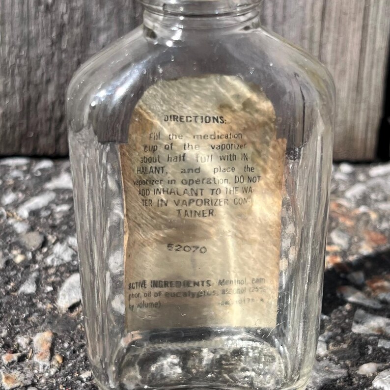 May include: A clear glass bottle with a label containing instructions and ingredient information. The label text includes "DIRECTIONS" and "ACTIVE INGREDIENTS". The bottle has a vintage aesthetic.