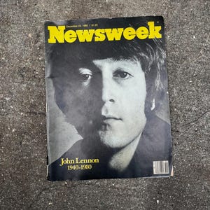 Pode incluir: Uma revista Newsweek vintage de 22 de dezembro de 1980, com um retrato em preto e branco de John Lennon na capa. O cabeçalho amarelo diz Newsweek, e o texto abaixo do retrato indica John Lennon 1940-1980 com um código de barras.