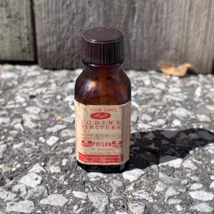 Op de afbeelding: Een kleine, vintage bruine glazen fles met een donkerbruine dop. Het etiket luidt "Hall Iodine Tincture" en bevat het woord "POISON". De fles bevat 1/2 fluid ounce vloeistof en is een antisepticum voor uitwendig gebruik.