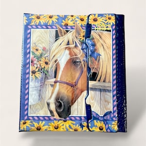 May include: A white ceramic mug with a black handle and the text "But First, Coffee" in a bold, black font. The mug is set against a blurred background, suggesting a cozy setting.