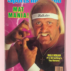 May include: A vintage Sports Illustrated magazine cover from April 29, 1985, featuring wrestler Hulk Hogan. The cover has a pink background with the text "MAT MANIA!" and "Hulkster" on a white headband. Hogan is wearing a cross necklace.