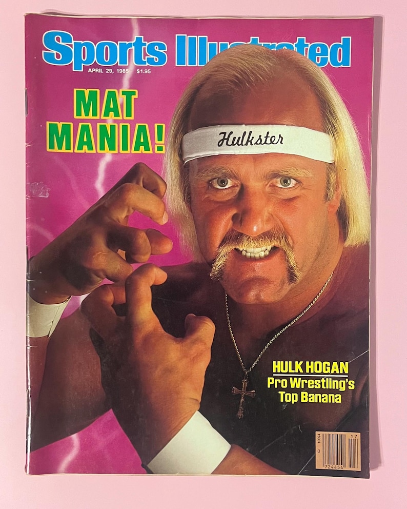 May include: A vintage Sports Illustrated magazine cover from April 29, 1985, featuring wrestler Hulk Hogan. The cover has a pink background with the text "MAT MANIA!" and "Hulkster" on a white headband. Hogan is wearing a cross necklace.