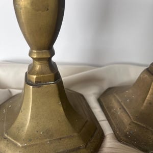 May include: Two antique brass candlesticks with a hexagonal base and a fluted column. The candlesticks have a warm, aged patina, suggesting they are vintage. The background is a neutral color.