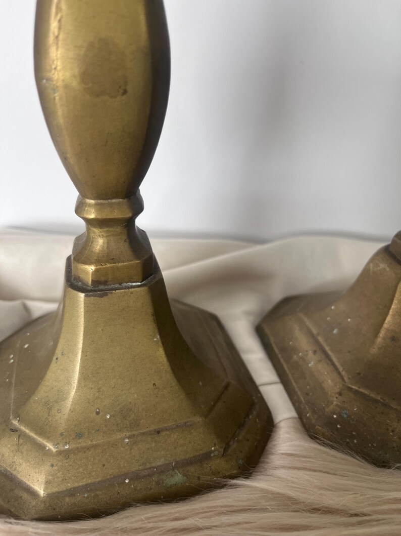 May include: Two antique brass candlesticks with a hexagonal base and a fluted column. The candlesticks have a warm, aged patina, suggesting they are vintage. The background is a neutral color.