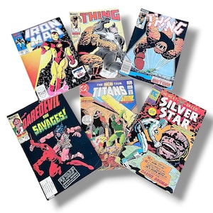 Op de afbeelding: Een verzameling vintage stripboeken met Marvel- en DC-personages. Titels zijn onder meer Iron Man, The Thing, Daredevil, The New Teen Titans en Silver Star. De covers tonen levendige illustraties en tekst.