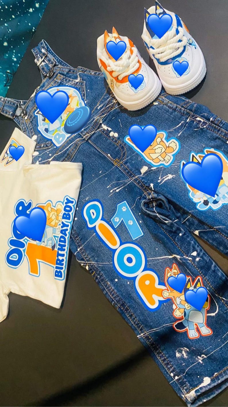 May include: A denim outfit set for a child, featuring a white t-shirt with "Birthday Boy" text and a number 1 graphic, denim overalls, and jeans with character graphics and paint splatter details. White and blue sneakers complete the ensemble.