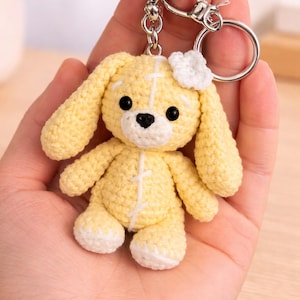 May include: A handmade yellow crochet bunny keychain with a white bow and black eyes. The bunny has long ears and a silver keychain ring. The bunny is approximately 3 inches tall.