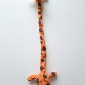 Könnte beinhalten: Ein langes, gehäkeltes Giraffenspielzeug mit einem leuchtend orangefarbenen Körper und dunkelbraunen Flecken. Die Giraffe hat einen sehr langen Hals, einen kleinen Kopf mit zwei kleinen Hörnern und eine abgerundete Basis mit vier kurzen Gliedmaßen.