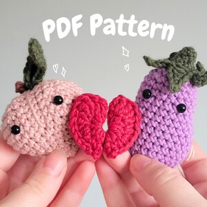 May include: Crocheted amigurumi vegetables, including a pink radish, a red heart, and a purple eggplant, with black button eyes. The text "PDF Pattern" is displayed above the objects. The radish and eggplant have green crocheted tops.