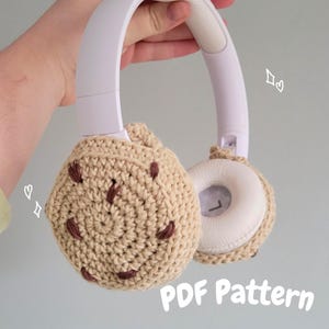 Peut inclure: Casque audio blanc avec des coussinets d'oreille en crochet beiges imitant des cookies aux pépites de chocolat. Détails marron cousus. Le texte "PDF Pattern" est visible. Accessoire fait main.
