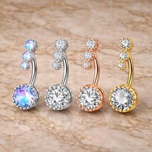 Piercing de umbigo pendente com três zircônias cúbicas, em aço cirúrgico, nas cores ouro, prata e ouro rosa.