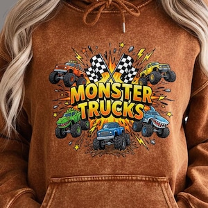 Pu&ograve; includere: Una felpa con cappuccio marrone con una grafica di monster truck. Il design include il testo "MONSTER TRUCKS" e immagini di vari monster truck, bandiere a scacchi e fulmini.