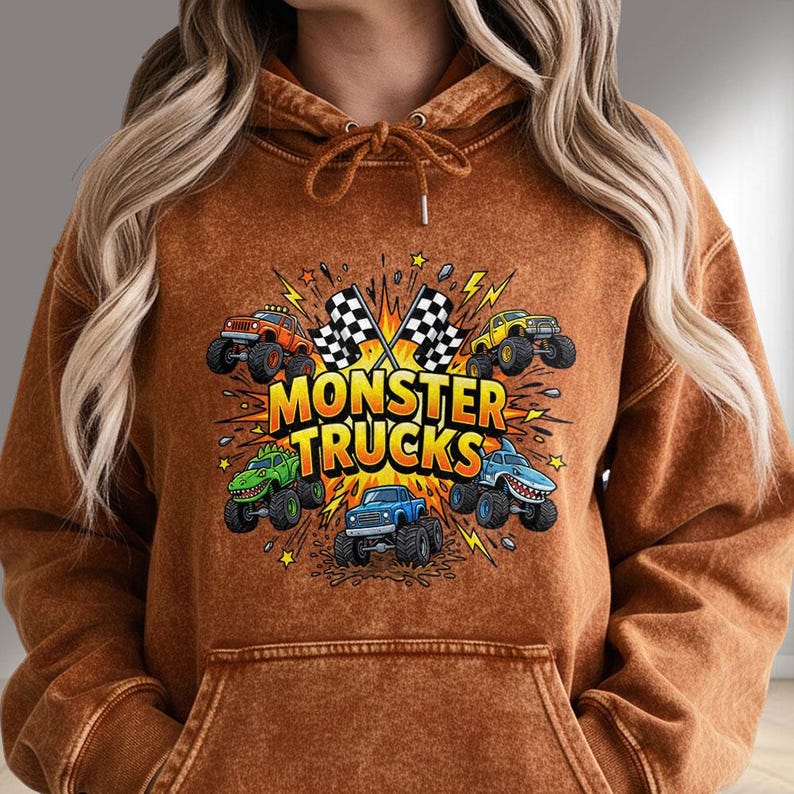 Pu&ograve; includere: Una felpa con cappuccio marrone con una grafica di monster truck. Il design include il testo "MONSTER TRUCKS" e immagini di vari monster truck, bandiere a scacchi e fulmini.