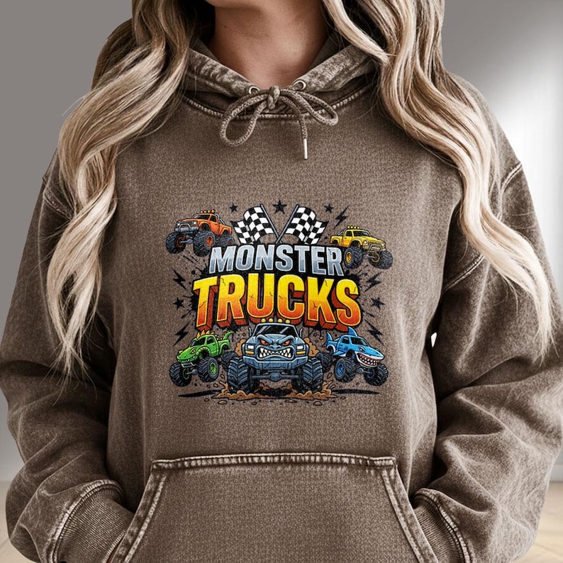 K&ouml;nnte beinhalten: Brauner Kapuzenpullover mit einem Front-Grafik-Design mit dem Text "MONSTER TRUCKS" und Illustrationen von Monster Trucks in verschiedenen Farben. Das Design umfasst karierte Flaggen und Sterne.