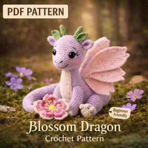 May include: A crocheted Blossom Dragon, a beginner-friendly pattern, sits on a bed of moss and flowers. The dragon is lavender with pink wings and a cream-colored belly. A crocheted flower rests in front of the dragon. The text "PDF Pattern" is at the top.