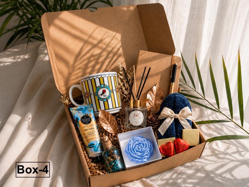 K&ouml;nnte beinhalten: Eine Geschenkbox mit der Aufschrift Box-4 enth&auml;lt eine gelb-wei&szlig; gestreifte Tasse mit Vogelmotiv, eine Handcremetube, einen Raumduft-Diffusor, ein Notizbuch mit Stift, eine blaue rosenf&ouml;rmige Kerze, zwei herzf&ouml;rmige Pralinen und blaue Hausschuhe.