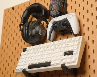 May include: A display of gaming accessories, including a white keyboard, black headphones, a white and black game controller, and a mouse with a colorful design. The items are mounted on a brown pegboard.