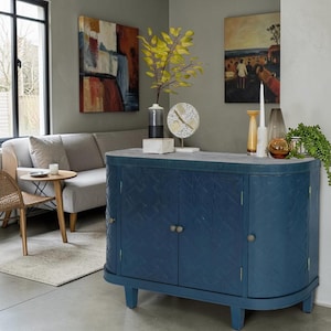 May include: A dark blue wooden sideboard with a light gray stone-like top, featuring three cabinet doors with a textured geometric pattern and small circular metal knobs, supported by short legs in a living room setting.