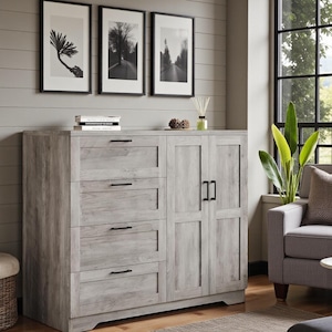 May include: A gray wooden dresser with five drawers on the left and two cabinet doors on the right. The dresser has black handles and is placed against a gray wall with three framed black and white pictures.