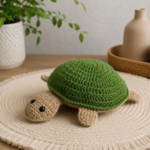 May include: A handmade crochet turtle with a green shell and tan body. The turtle has black button eyes and is sitting on a cream-colored placemat. The turtle is a decorative item.