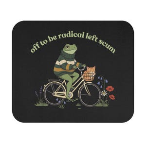 May include: Black mousepad with a whimsical illustration of a frog riding a bicycle with a cat in a basket. The frog wears a striped sweater, and the text "off to be radical left scum" is arched above the image. Flowers surround the bicycle.