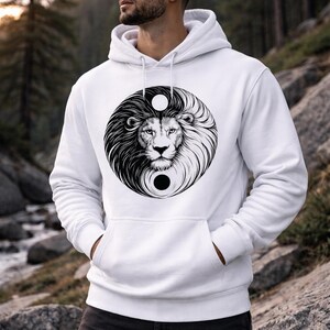 Puede incluir: Sudadera con capucha blanca con un diseño de león yin-yang en blanco y negro. La cara del león está centrada en el círculo, con una melena detallada. La sudadera tiene un bolsillo de canguro y una capucha con cordón.