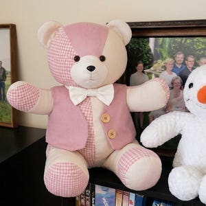 May include: A plush teddy bear with a patchwork design of pink gingham and solid cream fabric, wearing a pink vest with two wooden buttons and a white bow tie, positioned next to a white plush snowman with a bright orange carrot-shaped nose.