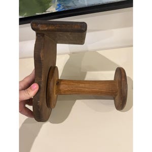 May include: A dark brown wooden wall-mounted paper towel holder featuring a flat rectangular top shelf and a horizontal cylindrical rod extending from a vertical back panel. The wood has a visible grain texture and a stained finish throughout.