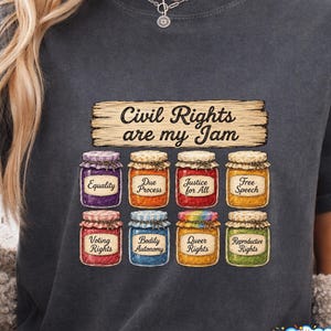 Op de afbeelding: Donkergrijs T-shirt met de tekst "Civil Rights are my Jam". De afbeelding toont illustraties van acht jampotten, elk gelabeld met een ander burgerrecht, zoals "Gelijkheid" en "Vrijheid van meningsuiting".