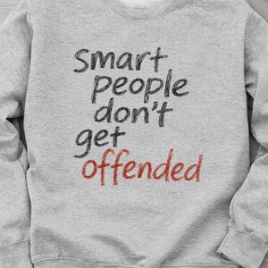 Op de afbeelding: Een lichtgrijs sweatshirt met de tekst "Smart people don't get offended" in zwarte en rode letters. De sweatshirt heeft een ronde hals en lange mouwen. De tekst staat in het midden van de voorkant.