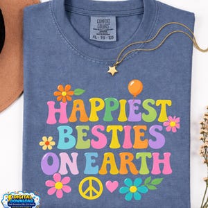 Peut inclure: Un t-shirt bleu Comfort Colors avec les mots "Happiest Besties On Earth" en lettres colorées de style rétro. Le motif comprend des fleurs, un symbole de paix, un cœur et un ballon. Un collier doré avec un pendentif en forme d'étoile est posé sur le t-shirt.