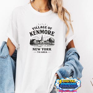 Peut inclure: T-shirt blanc avec un motif noir du village de Kenmore, New York, avec une église et des maisons. Le texte "VILLAGE OF KENMORE NEW YORK - 716 AREA -" est imprimé en dessous. Un graphique de téléchargement numérique est visible.