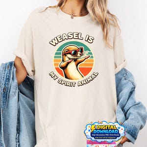 Puede incluir: Camiseta color crema con un dibujo de una comadreja con gafas de sol y el texto "WEASEL IS MY SPIRIT ANIMAL" en un diseño circular. La comadreja es marrón y naranja, sobre un fondo de puesta de sol retro.