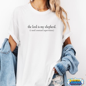 Peut inclure: T-shirt blanc avec l'inscription noire "the lord is my shepherd. (i need constant supervision.)". Le t-shirt est de style col rond.