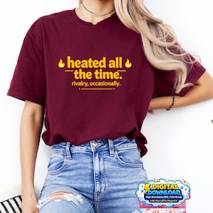 Peut inclure: Un t-shirt bordeaux avec le texte "heated all the time. rivalry, occasionally." en jaune. Le t-shirt est associé à un jean bleu. Le design comprend des graphiques de flammes. L'image contient également un graphique de téléchargement numérique.