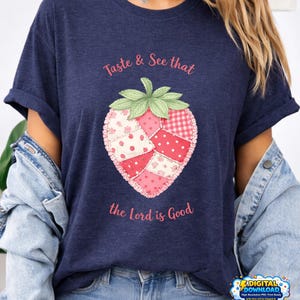 Peut inclure: T-shirt bleu marine avec une fraise en patchwork rose et rouge et l'inscription "Taste & See that the Lord is Good". Les manches sont retroussées.