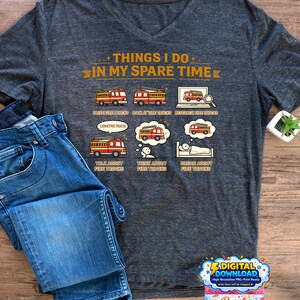 Peut inclure: T-shirt gris foncé à col en V avec le texte "THINGS I DO IN MY SPARE TIME". Le t-shirt présente des illustrations de camions de pompiers et d'activités connexes. Un jean bleu est plié à côté du t-shirt.