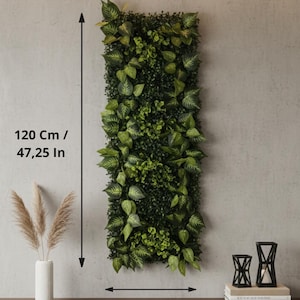May include: A rectangular vertical artificial plant wall, 47.25 inches tall and 15.75 inches wide, with various shades of green foliage. The wall is mounted on a light gray wall. A brown wooden shelf below holds a white vase with pampas grass and black candle holders.