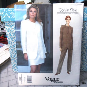May include: Vogue Patterns sewing pattern featuring Calvin Klein designs. The pattern includes a white suit with a long jacket and skirt, and a brown suit with a jacket and pants. The pattern number is 1553, and the size range is 12-14-16.