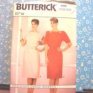 May include: A Butterick sewing pattern showing two dresses, one white with a bow, the other red. The pattern is size 10, designed by David Warren. The package has a blue floral background.