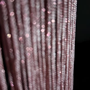 Peut inclure: Une s&eacute;rie de brins verticaux de couleur rose poudr&eacute; dot&eacute;s d'une subtile finition m&eacute;tallique scintillante. La texture se compose de fils fins et &eacute;troitement tiss&eacute;s cr&eacute;ant un motif lin&eacute;aire, refl&eacute;tant la lumi&egrave;re avec des reflets bokeh doux.