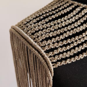 Peut inclure: Un accessoire d'&eacute;paule dor&eacute; m&eacute;tallique compos&eacute; d'une s&eacute;rie de cordons tress&eacute;s horizontaux reli&eacute;s &agrave; un bord &eacute;pais et structur&eacute;. De longues franges dor&eacute;es, droites et scintillantes, pendent verticalement depuis le bord ext&eacute;rieur.