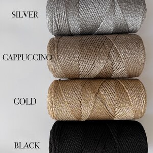 Peut inclure: Quatre bobines cylindriques de cordon m&eacute;tallique dispos&eacute;es verticalement. Les couleurs sont &eacute;tiquet&eacute;es SILVER, CAPPUCCINO, GOLD et BLACK. Chaque bobine pr&eacute;sente une texture tress&eacute;e &eacute;troitement enroul&eacute;e avec un &eacute;clat distinct.