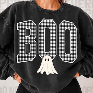 Könnte beinhalten: Ein anthrazitfarbenes Sweatshirt mit Rundhalsausschnitt, das das Wort BOO in großen Blockbuchstaben mit einem schwarz-weißen Büffelkaromuster zeigt. Unter dem Buchstaben O befindet sich eine kleine, einfache weiße Geisterillustration mit zwei schwarzen Augen.
