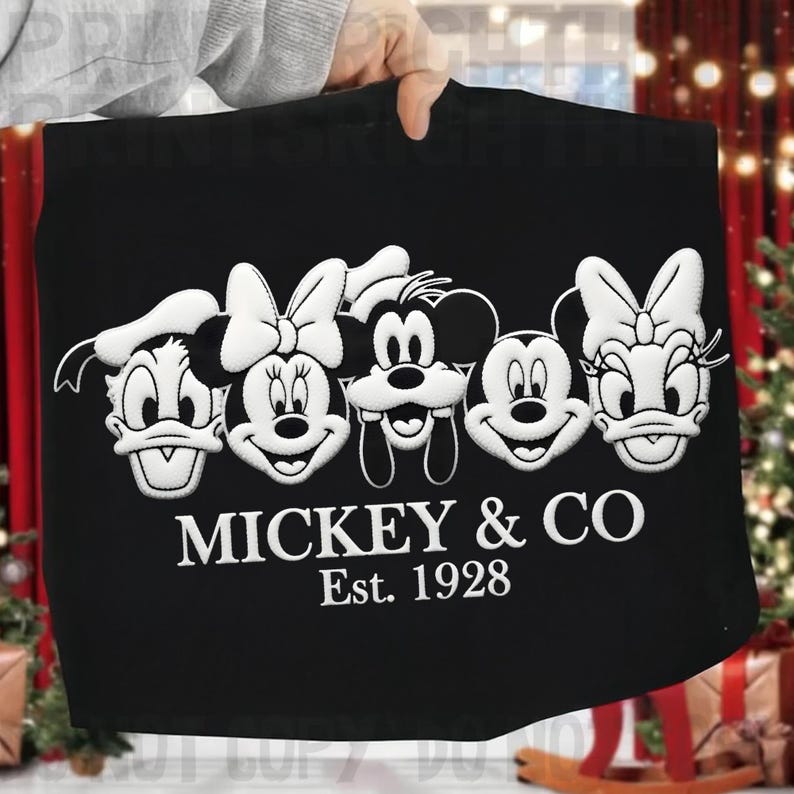 May include: Black tote bag featuring embroidered images of Disney characters: Donald Duck, Minnie Mouse, Mickey Mouse, and Daisy Duck. The text "MICKEY & CO Est. 1928" is embroidered below the characters. The bag is held up by a person.