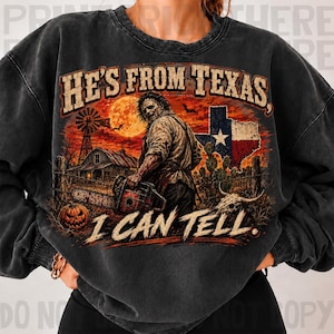 Puede incluir: Una sudadera gris carb&oacute;n de cuello redondo con un estampado gr&aacute;fico de un personaje de pel&iacute;cula de terror sosteniendo una motosierra. El dise&ntilde;o incluye un granero, un molino, una calabaza, la bandera de Texas y el texto HE'S FROM TEXAS, I CAN TELL.