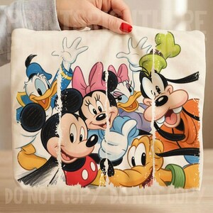 May include: A cream-colored tote bag featuring a colorful graphic of Disney cartoon characters, including Mickey Mouse, Minnie Mouse, Donald Duck, Daisy Duck, and Goofy. The image has a distressed, vintage look.